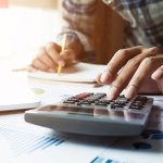 man hand holding pen working on calculator and laptop